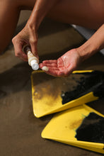 Load image into Gallery viewer, Dresden Holden acupuncturist in santa barbara made Wipe Out. Photo is of a person using Wipe out beach tar remover at the ocean, squeezing it out a plastic bottle into her hand over a pair of boogie board flippers. Wipe out is shown as a nontoxic clean beach tar remover for santa barbara beaches. 2 ounce plastic bottle with a no mess cap and a brown label that says Wipe Out!
